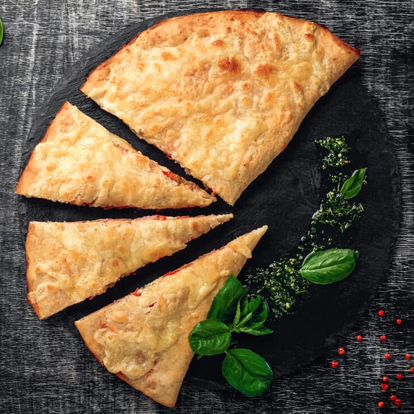 Tank's Pizza calzone, sliced into pieces, with pesto and basil on a dark slate.