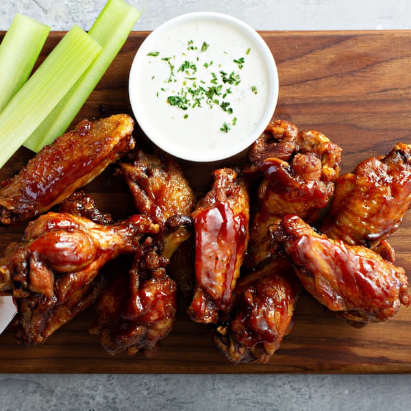 Tank's Pizza BBQ chicken wings with ranch dipping sauce and celery sticks on a wooden board.