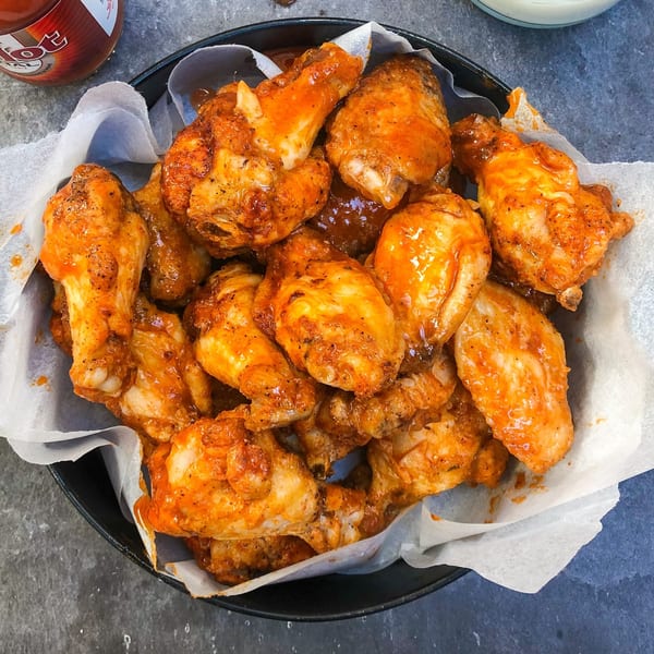 A black bowl filled with Tank's Pizza's buffalo chicken wings, coated in a vibrant orange sauce.