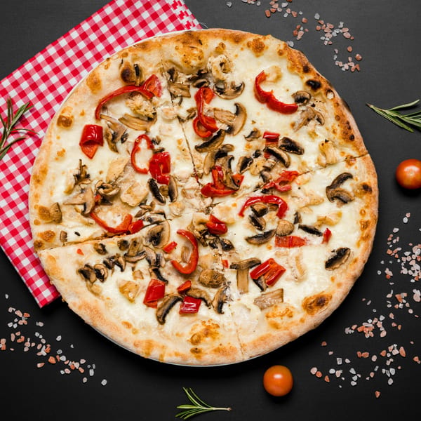 Tank's Pizza with white sauce, mushrooms, red peppers, and chicken on a black background.