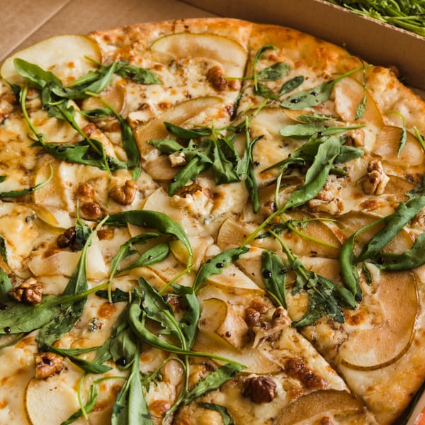 Tank's Pizza with pear slices, walnuts, arugula, and balsamic glaze in a pizza box.
